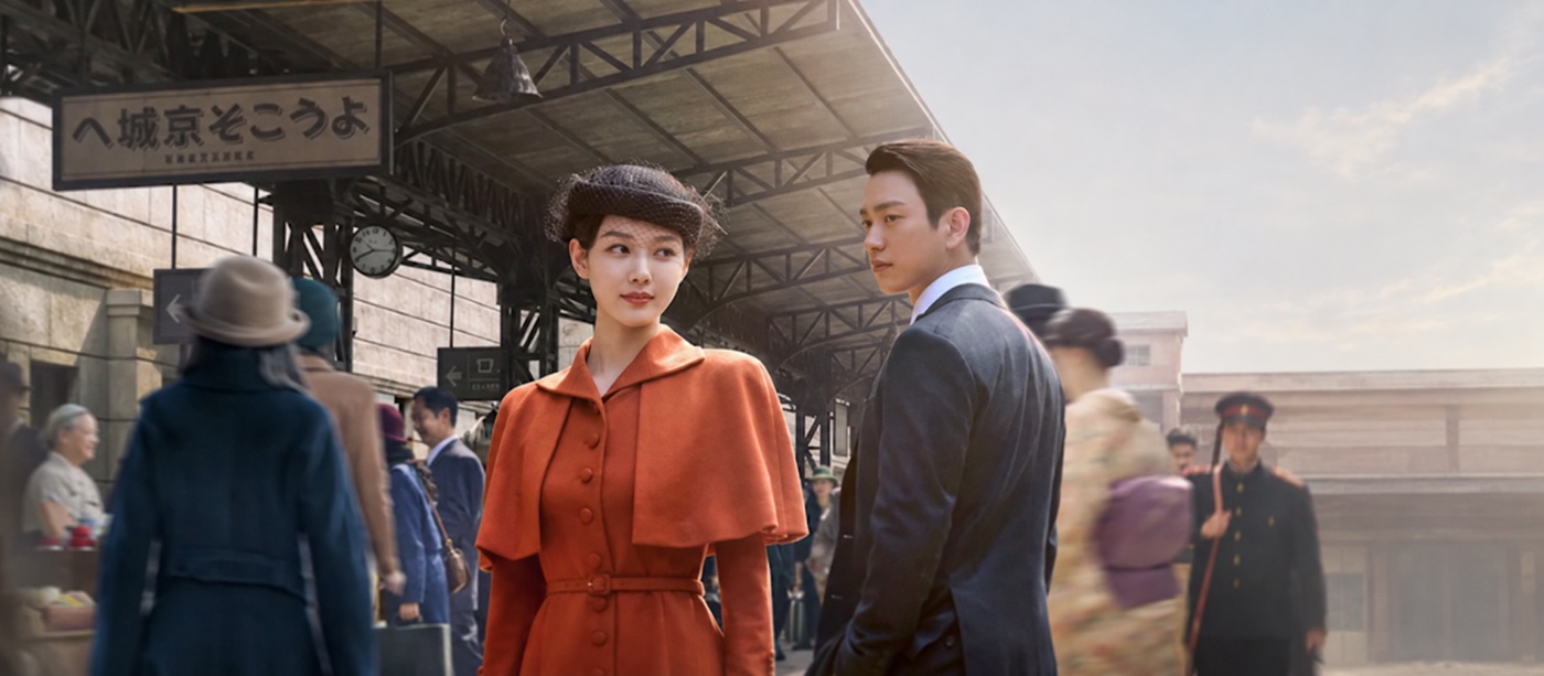 100 Days of Deception article cover showing a woman in an orange outfit and a man in a dark suit at a period railway station