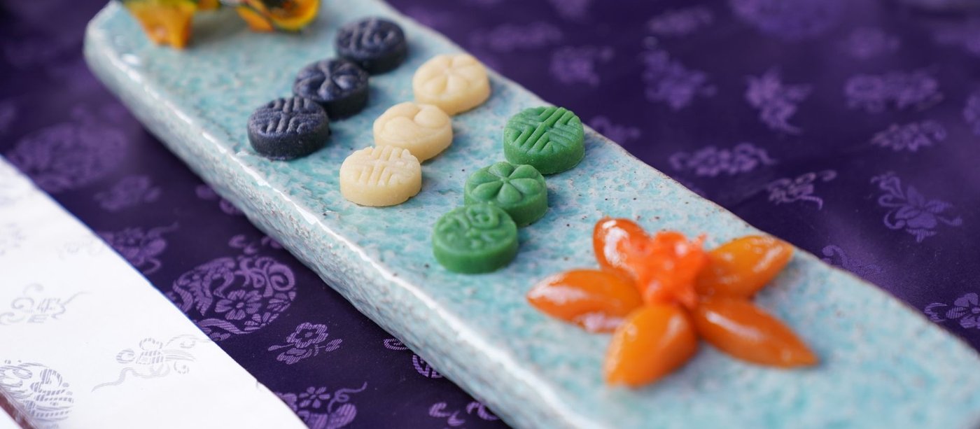 Hangwa, a Chuseok food: patterned dasik tea cookies in black, cream and green beside a flower-shaped sweet on a celadon plate