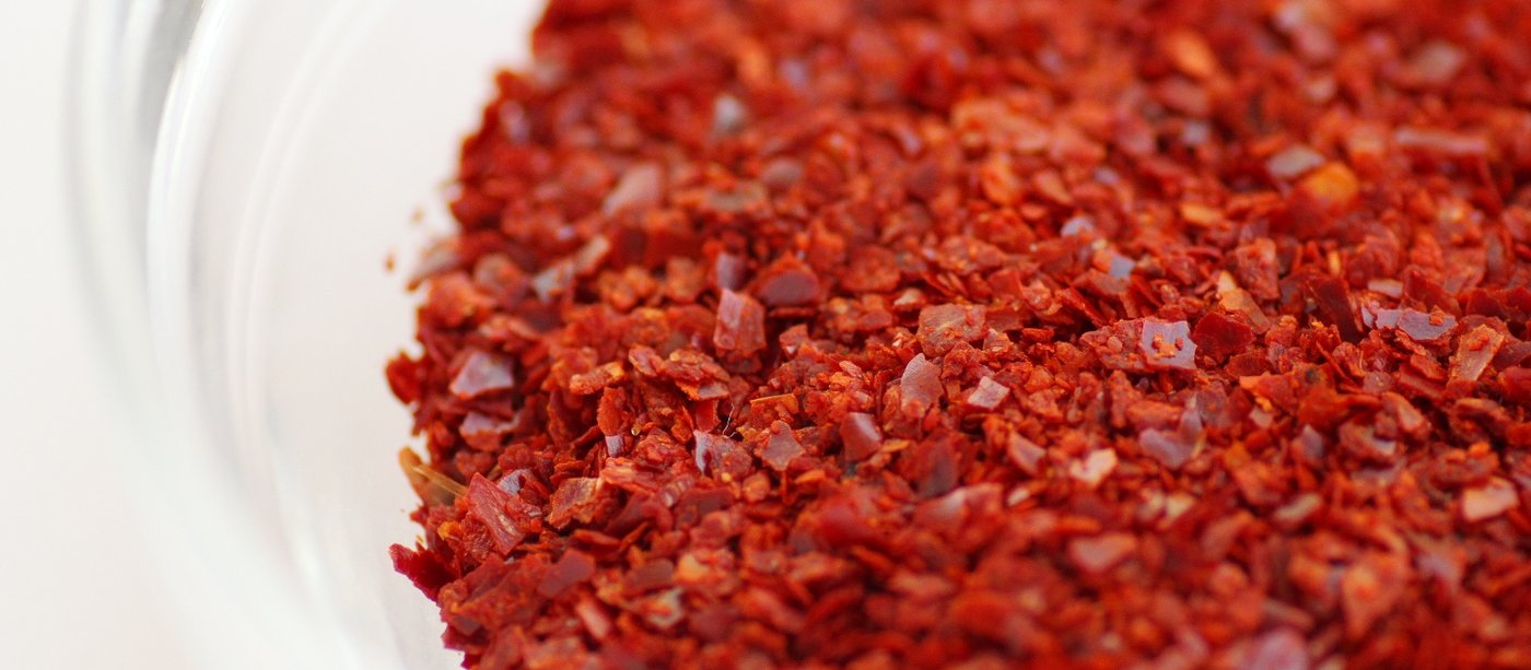 Coarse Korean gochugaru chili flakes piled in a glass bowl, deep red with visible seed and pepper texture.