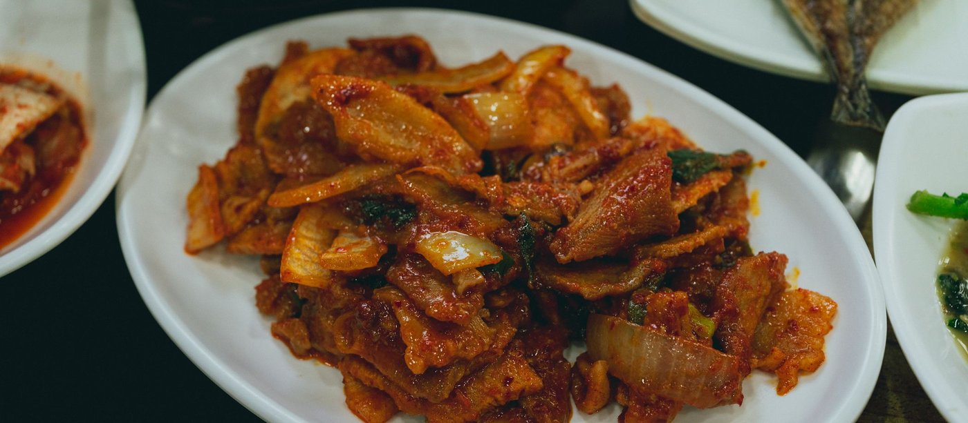 Stir-fried kimchi glossy with gochujang on a white plate, surrounded by small banchan dishes