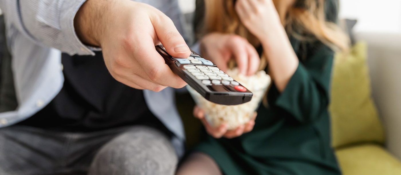 How many episodes are in a kdrama: a hand points the TV remote while a friend reaches into a bowl of popcorn on the sofa