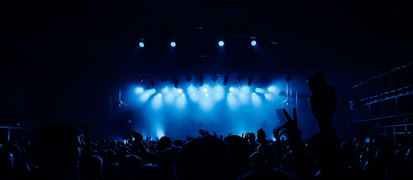 A concert crowd in silhouette facing a stage washed in blue light before a K-pop comeback show