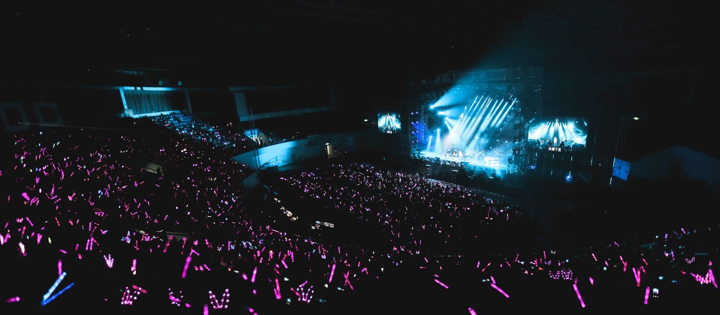 An arena crowd waving hundreds of pink light sticks toward a blue-lit concert stage