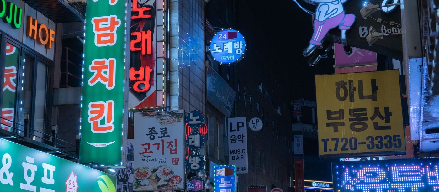 Neon hangul signs stacked up a building facade on a Seoul street at night
