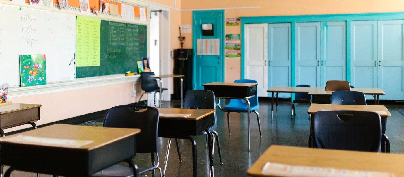 An empty classroom with wooden desks and a green chalkboard